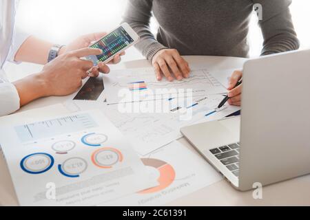 Business team two colleagues working with computer, mobile, discussing and analysis graph stock market trading with stock chart data, financial and in Stock Photo