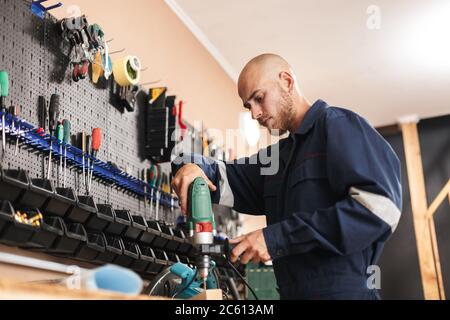 Young foreman in work clothes using electric drill with stand of Stock Photo