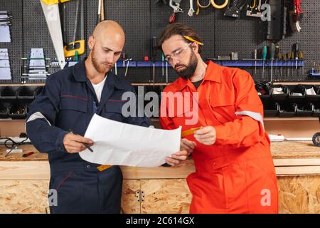Two builders in work clothes thoughtfully looking on sketch with Stock Photo