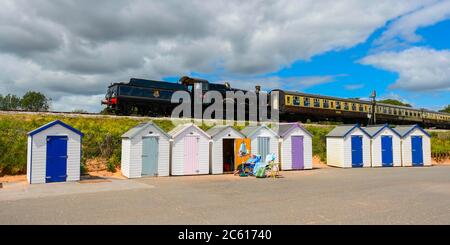 Goodrington Sands, Paignton, Devon, UK.  6th July 2020.  The Dartmouth Steam Railway reopens with a passenger train hauled by 7827 Lydham Manor passing behind the beach huts at Goodrington Sands on its trip to Kingswear after leaving the station at Paignton in Devon after the further easing of coronavirus lockdown rules allowed the heritage line to carry passengers again.  Picture Credit: Graham Hunt/Alamy Live News Stock Photo