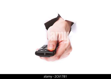 male hand with tv remote control presses the shutdown button through a hole in paper on a white background isolate. close up, copy space. Stock Photo