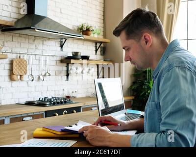 Work from home concept. A young man works with documents in the kitchen. Stock Photo