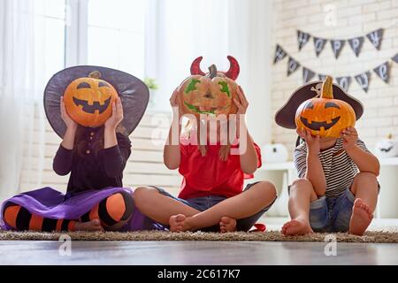 Happy brother and two sisters on Halloween. Funny kids in carnival costumes indoors. Cheerful children play with pumpkins and candy. Stock Photo