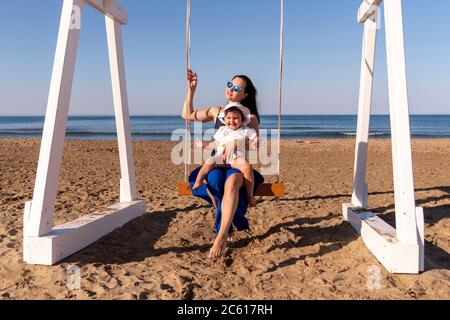 Beautiful woman swinging with her baby at the fine sandy Beach enjoying the idyllic scene of the sun and sea. Beautyful sandy beach in Antalya Stock Photo