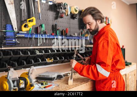 Foreman in work clothes thoughtfully using hammer with stand of Stock Photo