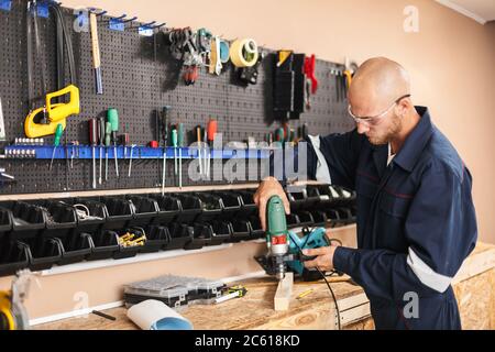 Young foreman in protective eyewear and work clothes using drill Stock Photo