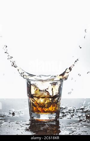 Rocks glass with whiskey in which ice drops splashing on a bar counter. Light background. Copy space Stock Photo