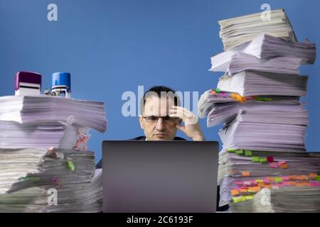 office worker swamped with documents doing overtime project on laptop computer Stock Photo