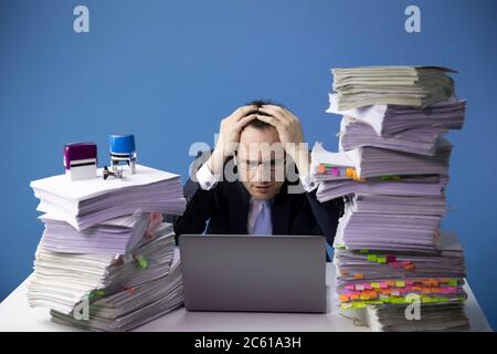 exhausted office employee doing overtime project amidst high stacks of documents Stock Photo