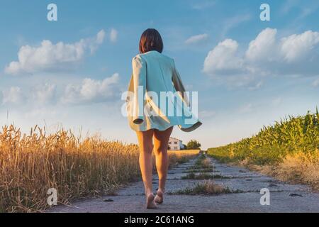 girl in a jacket at sunset goes on a country road Stock Photo