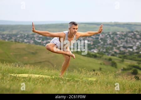 Sporty man doing yoga practice on mountain top. Peaceful guy enjoying his training surrounded by beautiful nature Stock Photo