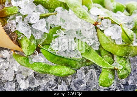 Frozen Edamame or soybeans in the mix with crushed ice on a blue background. Stock Photo