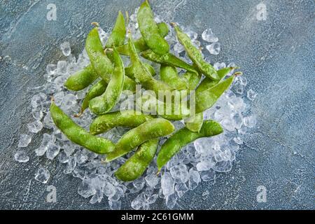 Frozen Edamame or soybeans in the mix with crushed ice on a blue background. Stock Photo