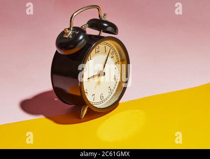 Black alarm clock with a hard shadow on a pink-yellow background. Stock Photo