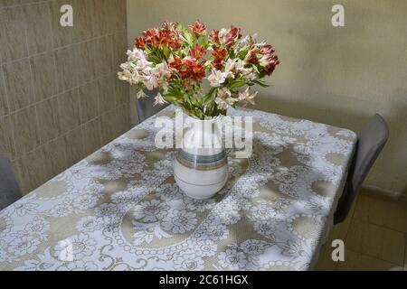 Vase. Astromelia flower vase, on a travertine marble table with a white lace tablecloth, scientific name Alstroemeria Hybrida, top-down view, Brazil, Stock Photo