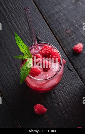 Fresh ice cold berry juice drink with mint, summer raspberry lemonade in glass with straws on dark wooden background, angle view Stock Photo