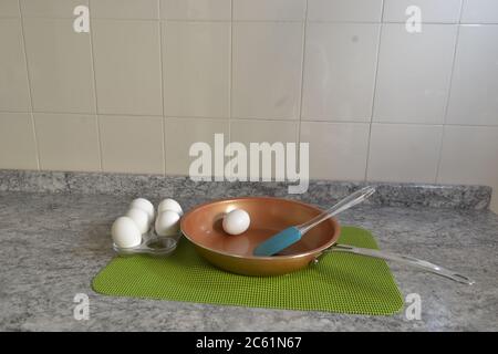 Frying pan with eggs still in their shell, to prepare on a green tablecloth, on a granite table and ceramic tile background, Brazil, South America Stock Photo