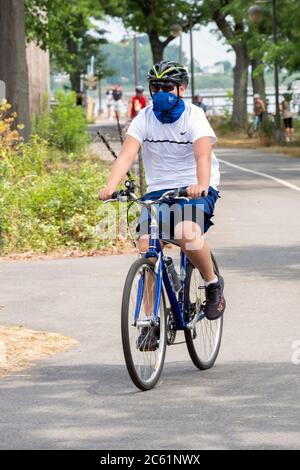 A man wearing a face scarf bandana cycles on a path near the Bayside Marina in Bayside, Queens, New York City. Stock Photo