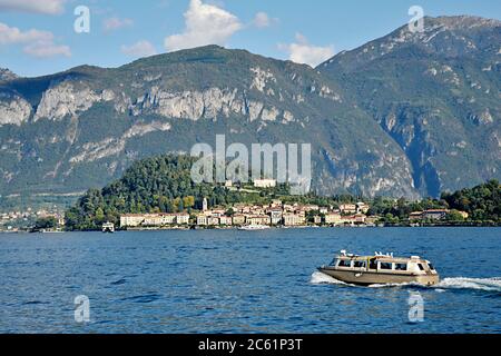 A holiday day trippers boat is heading towards a pretty village on Lake Como, Largo di Como, surrounded by the superb pre-alpine Mountains in spring Stock Photo