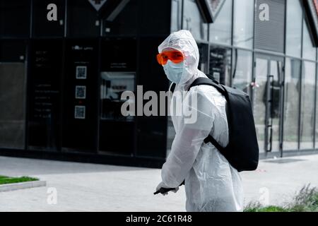 Man Riding Electric Kick Scooter Near Modern Buildings and Wearing Anti COVID Protective Suit, Glasses, Medicine Mask and Gloves Stock Photo