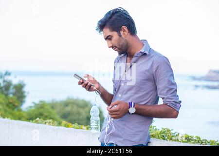 Side profile of a furious man watching apps on smart phone isolated  outdoors, on nature, sea on background Stock Photo