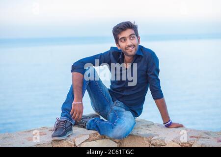 Man smiling looking to the side happy celebrating freedom while sitting on a concrete wall bridge above the sea. Positive person, peace mind concept. Stock Photo