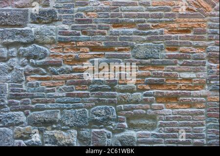 Multi-colored brick wall made with irregularly shaped bluish and red stones and boulders Stock Photo