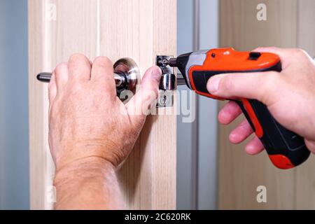 Repair of the door handle. The master clamps the loose screw with an electric screwdriver Stock Photo
