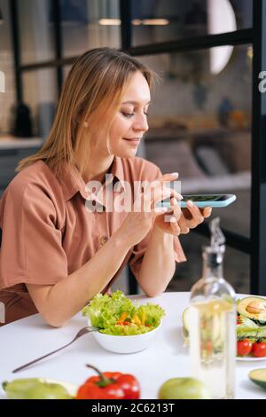 Blogger young woman uses smartphone for taking photos of vegetables. Stock Photo