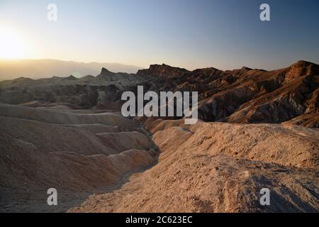 Sunset overlooking the golden and red coloured badlands at Zabriskie Point in Death Valley National Park, California. The sun rays shine over the view. Stock Photo