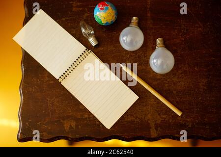 Open notebook, pen, globe and three light bulbs on a wooden table. View from above. Idea or inspiration concept. Stock Photo