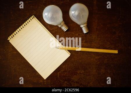 Open notebook with pen and two light bulbs on a wooden table. Flatlay. Idea or inspiration concept. Stock Photo