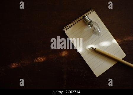 Notebook with pen and light bulb on a dark wooden table. Copy space. Stock Photo