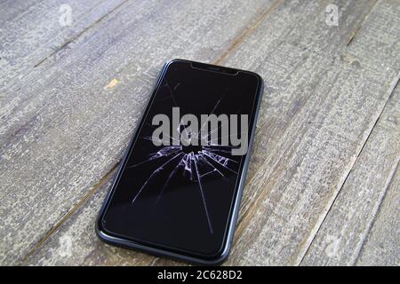 Viersen, Germany - July 6. 2020: Closeup of isolated mobile phone with cracked glass display on wood table Stock Photo