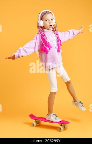 Active and happy girl with curly hair, headphones having fun with penny board, smiling face stand skateboard. Penny board cute skateboard for girls. Girl ride penny board yellow background. Stock Photo