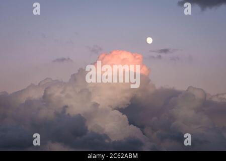 Top of a storm cloud turns pink after sunset. Bright moon shines in the sky. Stock Photo
