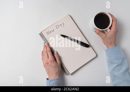 Notepad with text New day. Female hands holding cup of coffee on a white background. Top view. Stock Photo