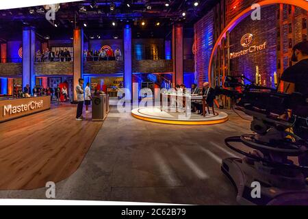 Two contestants of the cooking competition "MasterChef" stand at their workstations in a television studio in Cologne, Germany. The jury sits at an illuminated table beneath the show's round logo in the background, and an audience watches the recording from the gallery above. The German version of the format airs on Sky 1, produced by Endemol Shine Germany. Stock Photo