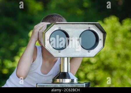 Boy looking through a tourist telescope on green Park background Stock Photo