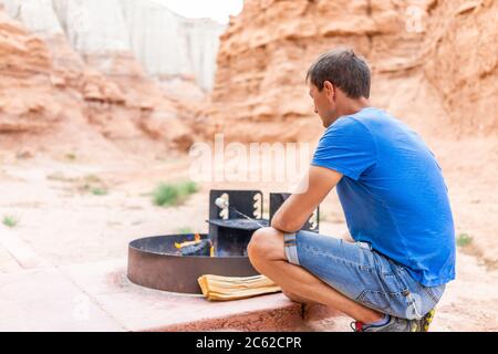Young man back roasting marshmallows on fire in campground campfire grill in desert landscape in Goblin Valley State Park in Utah Stock Photo