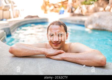 Young man happy looking at camera swimming in Japanese spa in Japan onsen hot spring pool with bokeh background blue water leaning on edge Stock Photo
