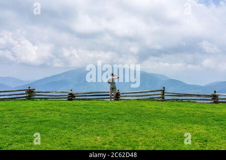 Devil's Knob Overlook with photographer man in green grass lawn field meadow and fence at Wintergreen resort town village near Blue Ridge parkway moun Stock Photo