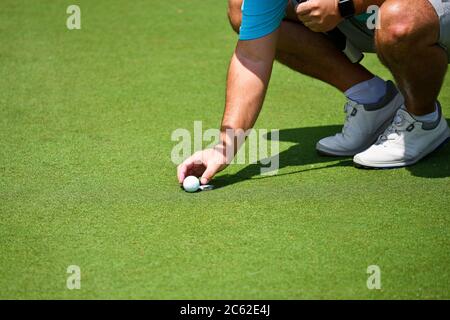 Young Man Kneeling Down and Placing his Golf Ball and Marker on the Putting Green. Stock Photo