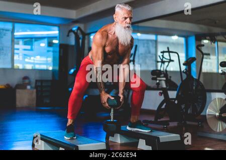 Hipster senior man training inside gym - Mature tattooed person having fun doing workout exercises in sport fitness club - Active elderly lifestyle an Stock Photo