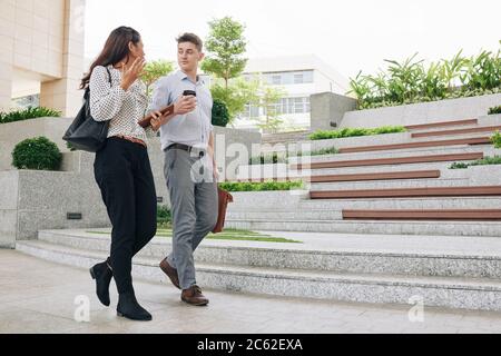 Emotional young businesswoman actively gesturing and talking to colleague when thay are walking in the street Stock Photo