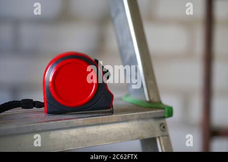 Red construction tape measure lies on the step of the ladder Stock Photo
