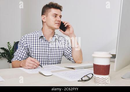 UI designer making corrections in design when talking on phone with customer Stock Photo