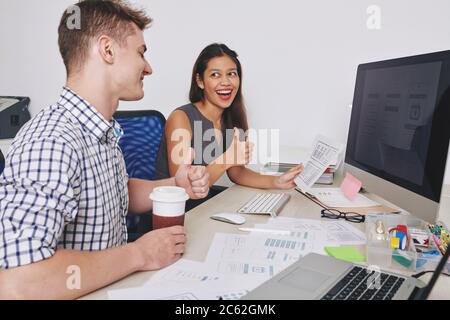 Happy excited young UI designer showing mobile application interface mock-up too colleague and showing thumbs-up Stock Photo