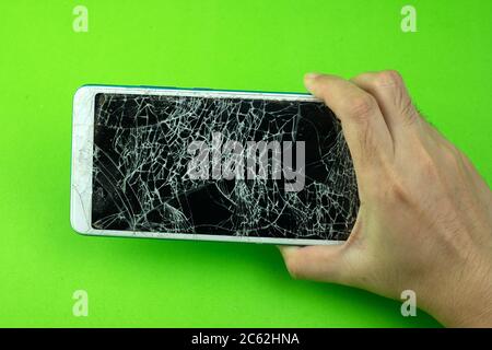 Hand holding smartphone screen is cracked on green background Stock Photo