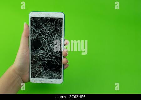 Hand holding smartphone screen is cracked on green background Stock Photo
